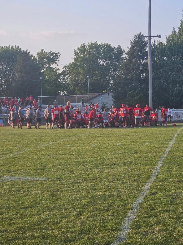 Football team in red jerseys gathered for a huddle on a grassy field during a practice session.