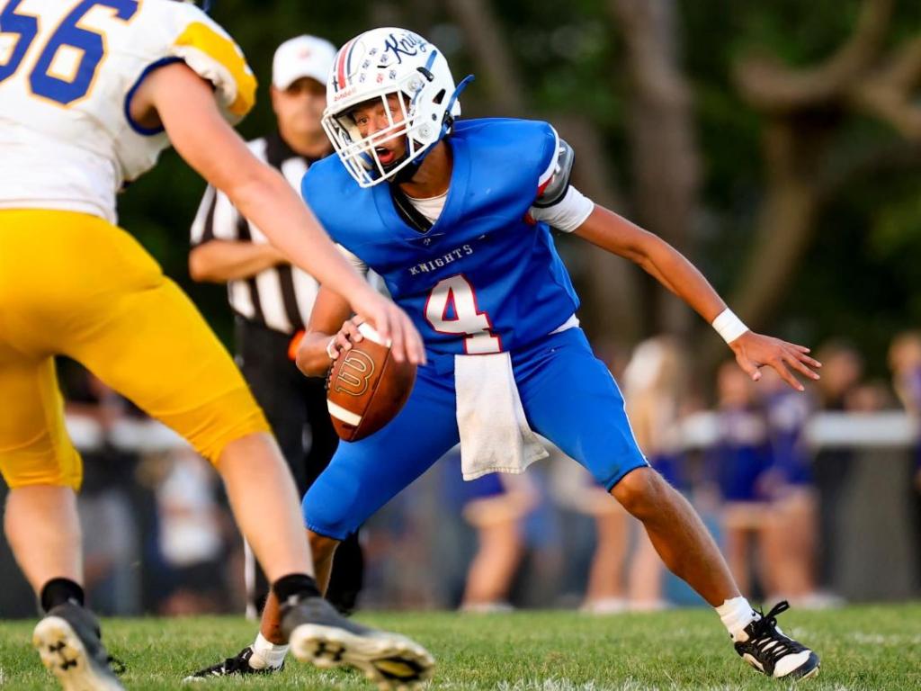 A Crestview Knights football player in blue uniform number 4 prepares to pass the ball while being pressured by a player from the opposing team in yellow.