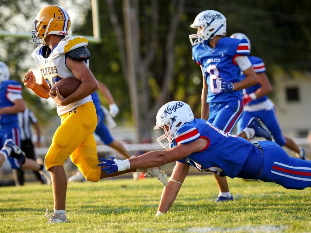 A football player in a yellow jersey evades a tackle from a blue jersey player on a grassy field during a game.