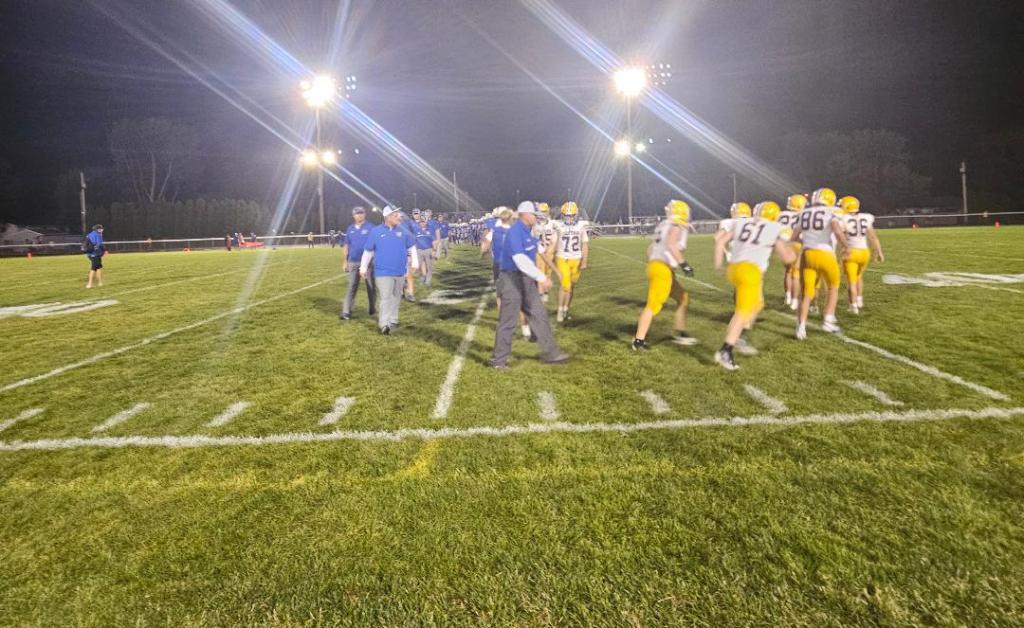 A group of Crestview Knights football players in yellow and gray uniforms walk off the field under bright stadium lights after a game.