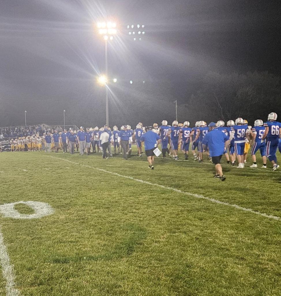 Players from the Crestview Knights football team walking on the field during a night game, with stadium lights shining.