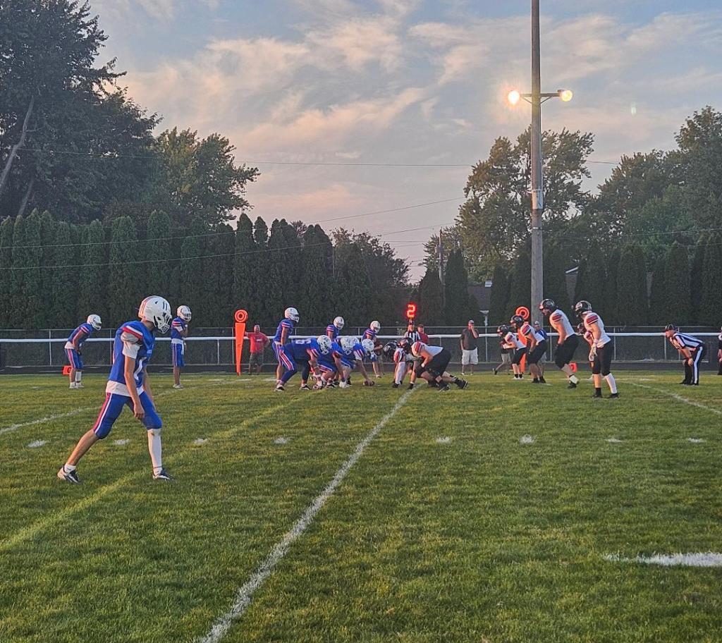 High school football game in Convoy, Ohio, with players on the field preparing for a play under a colorful sunset.