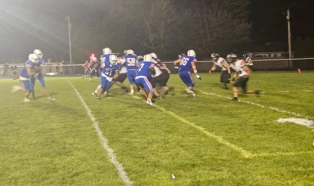 A high school football game in progress, showing players from two teams on the field during a night game.