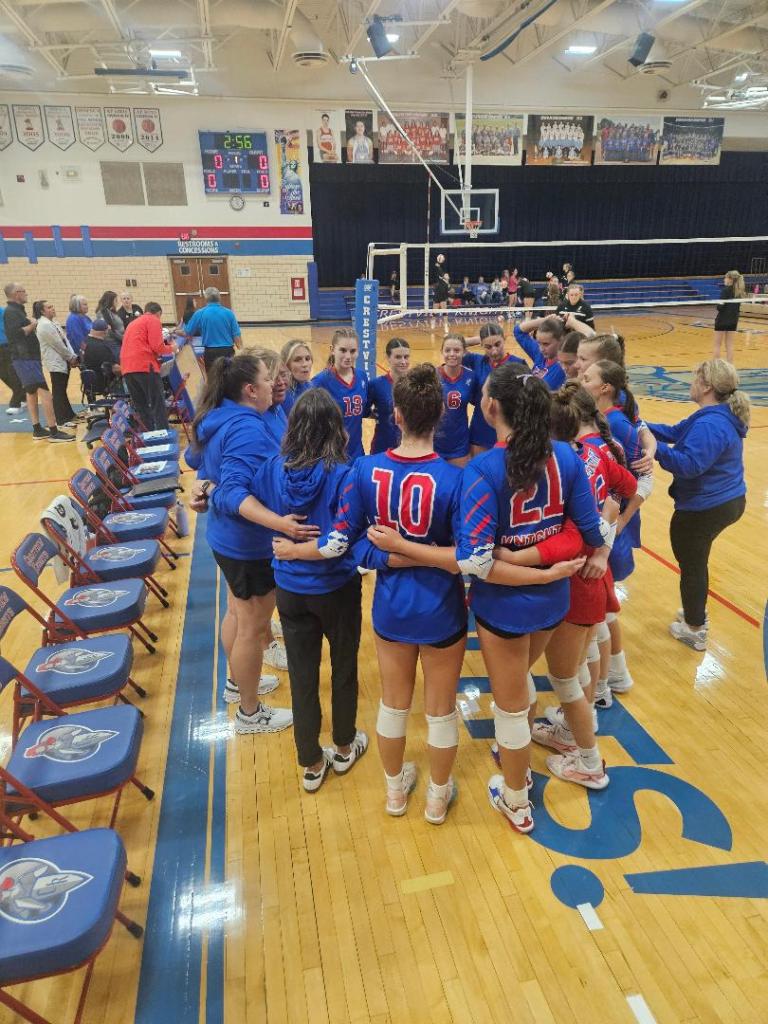 Crestview Lady Knights Volleyball Team huddled together on the court before a match, wearing blue uniforms and preparing for the game.