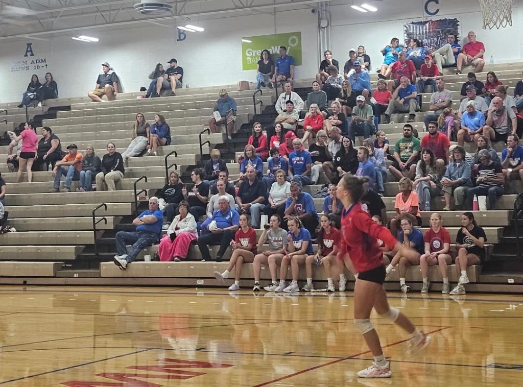 A volleyball player from the Crestview Lady Knights prepares to serve during a match against the Spencerville Bearcats, with an audience visible in the background.