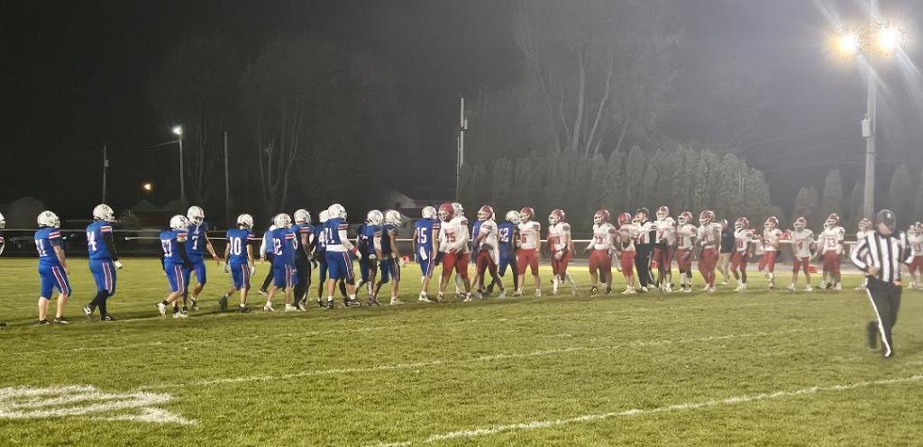 Crestview Knights and Lima Central Catholic Thunderbirds players shaking hands after a competitive football game under night lights.