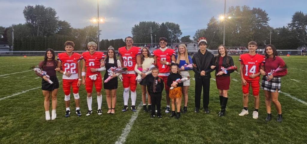 Group of high school students in football uniforms and formal attire during a homecoming ceremony on a football field.