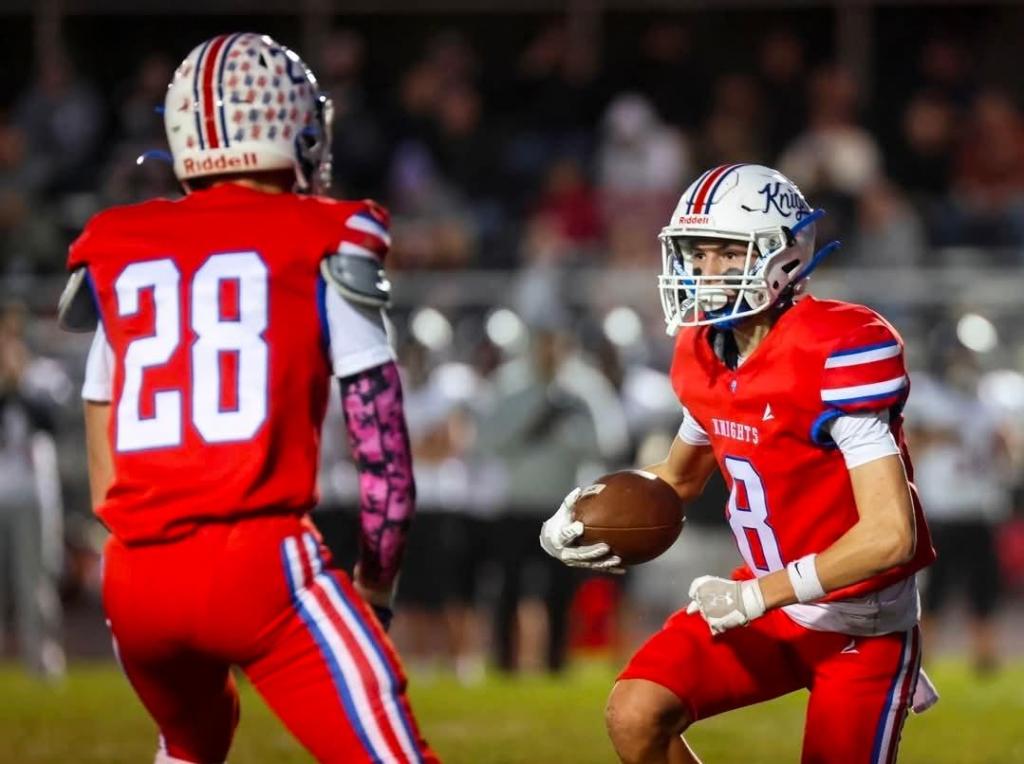Two football players in red uniforms, one (#28) facing away and another (#8) holding a football while looking determined, set against a night game backdrop.