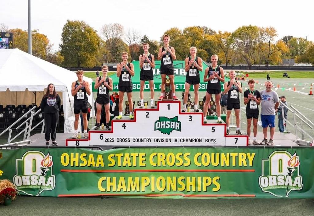 Crestview Knights cross country team celebrating their victory on the podium at the OHSAA State Championships, with the championship banner displayed.