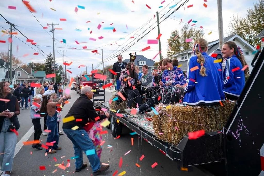 A celebratory parade scene with the Crestview Knights cross country team on a float, surrounded by confetti and a cheering crowd.