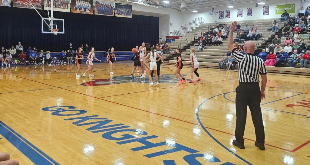 A basketball game is in progress at Crestview High School, featuring the Lady Knights and the Fort Jennings Lady Musketeers. A referee is making a call as players are positioned on the court, with spectators visible in the background.