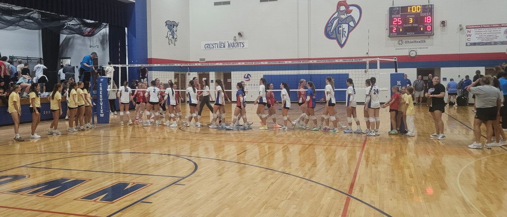 A volleyball match conclusion, with players shaking hands at the net. The scoreboard shows a final score of 25-18. Teams in yellow and red/white uniforms are visible in a gymnasium setting.